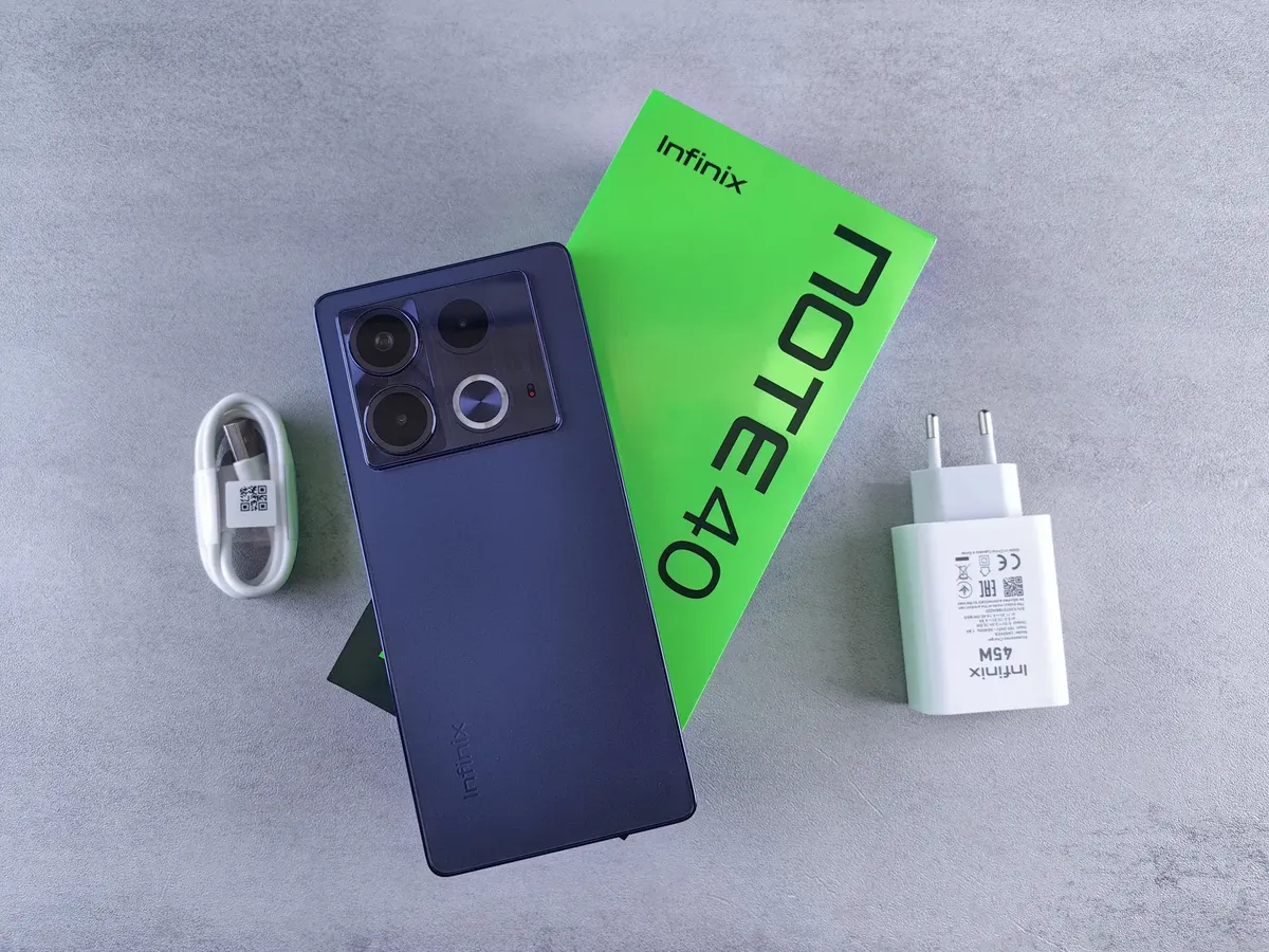 Unboxing of Infinix Note 40 showing the phone, charger, and USB cable on a gray surface.